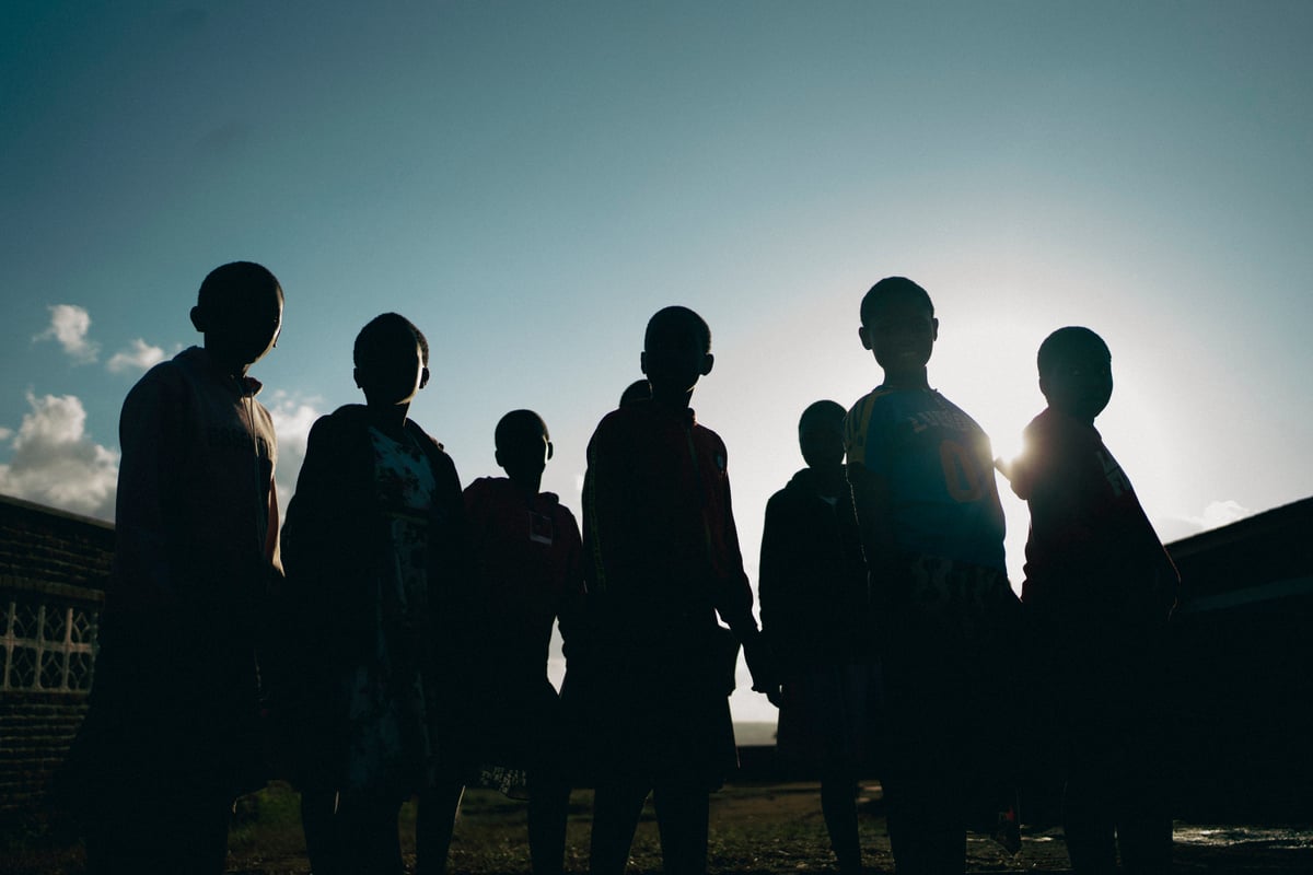 Siluetas de un grupo de niños y niñas a contraluz bajo un cielo azul.