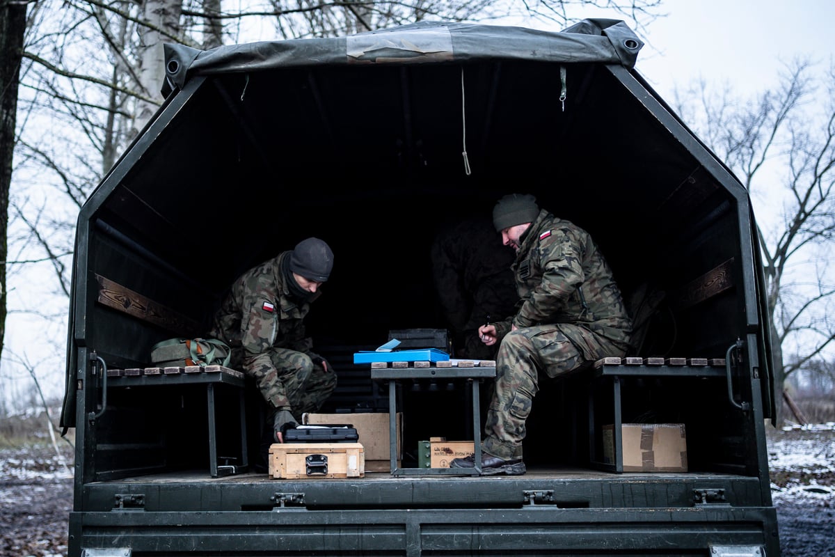 Dos soldados trabajan sentados en la caja abierta de un camión militar en invierno.
